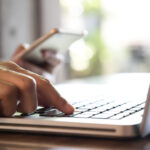 Hands holding mobile phone and using laptop. Online shopping