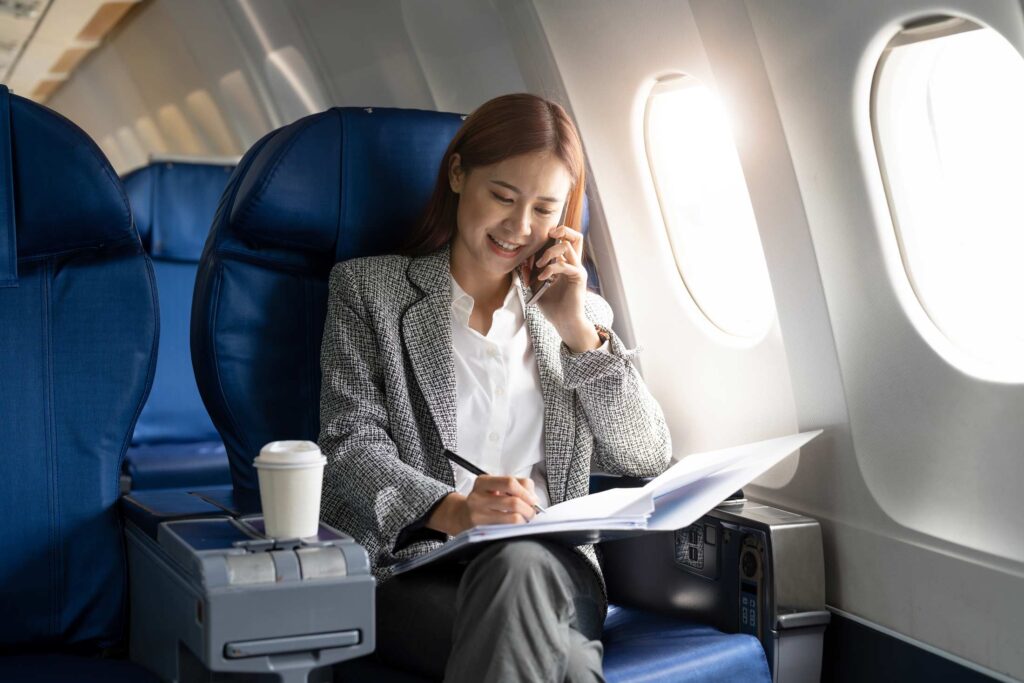 Business young asian woman talking on phone during working for paperwork financial report on airplane, flight in plane