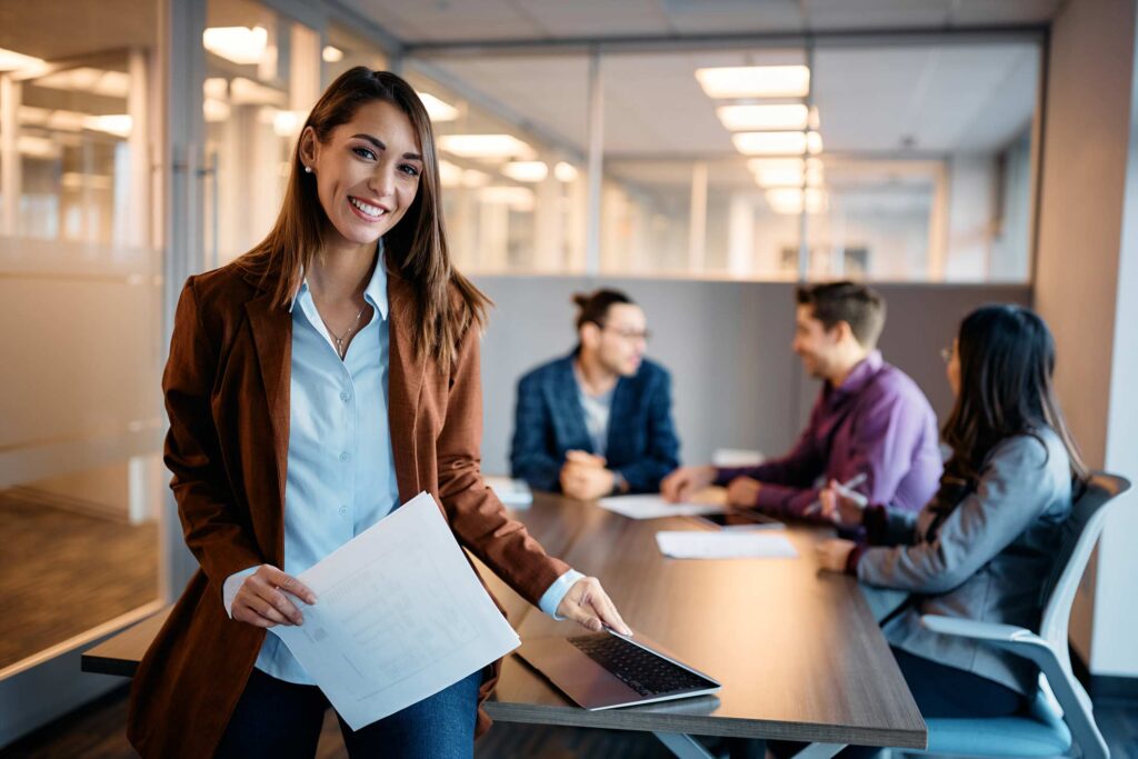 Happy businesswoman having meeting with coworkers in office and looking at camera.
