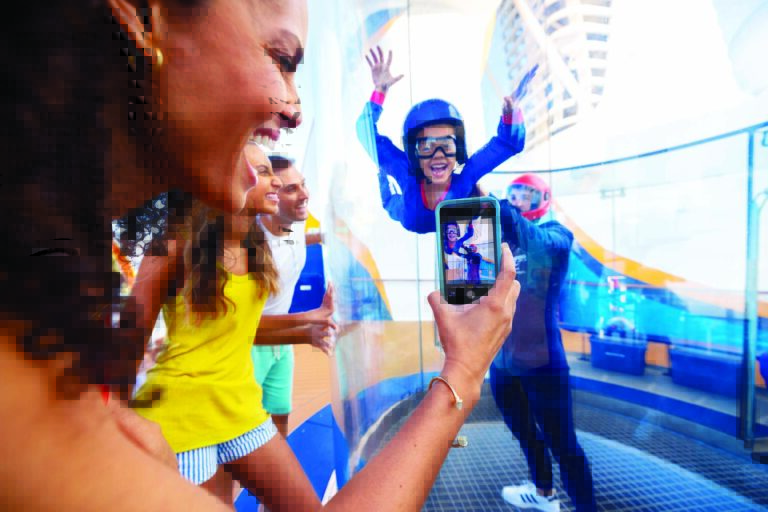 OY, Odyssey of the Seas, friends and family, mother daughter left side, watching young boy in Ripcord by Ifly, big smile on kid, fun, action, excitement, staff attendant helping child, onboard skydiving simulation, mom close frame left side, taking a photo,