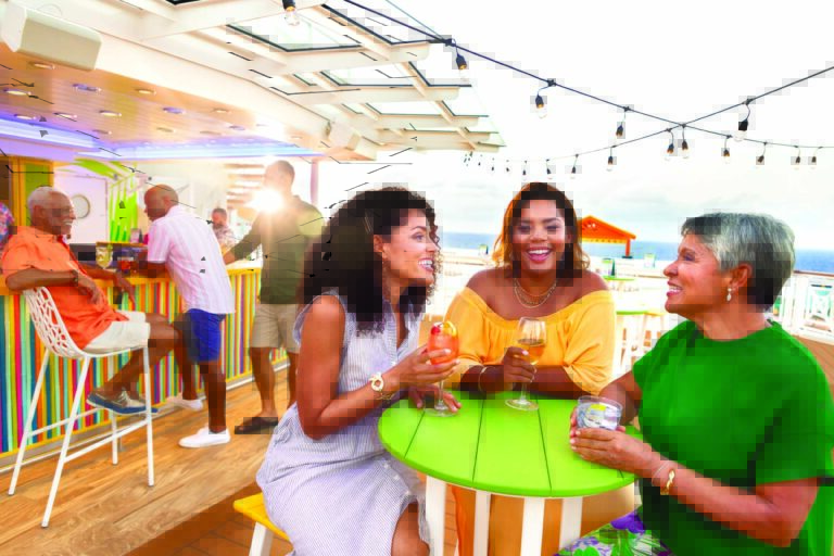 OY, Odyssey of the Seas, Lime & Coconut, three women enjoying drinks at table, laughing, sunset, people seated at bar in background, friends,