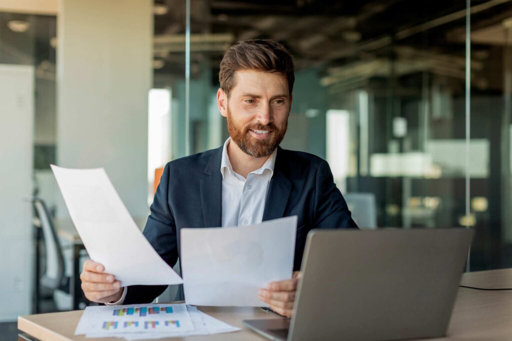 Busy male entrepreneur working with laptop and documents in office