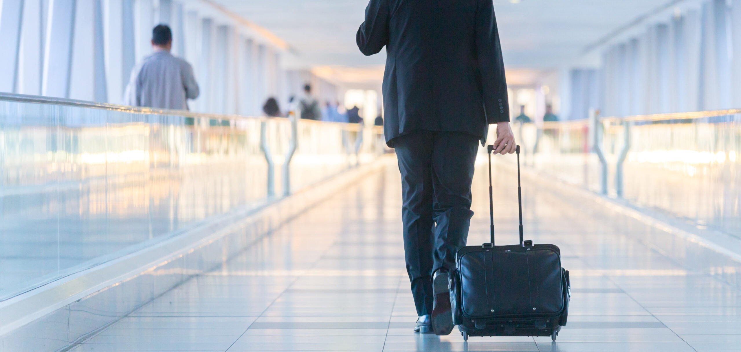 Businessman walking and wheeling a trolley suitcase at the lobby, talking on a mobile phone. Business travel concept.