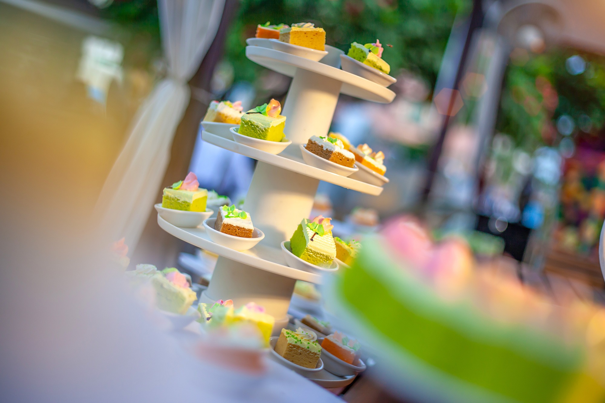 A tower of different pieces of cake on a buffet table in a tropical setting