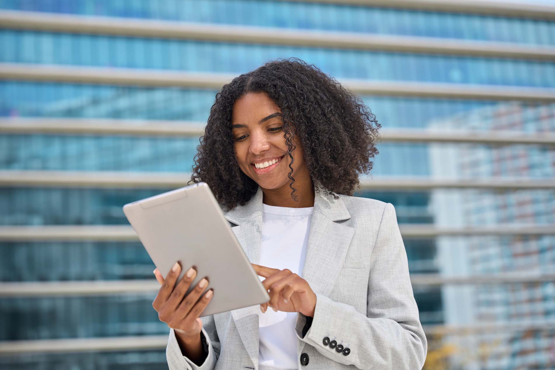 Young business woman holding a tablet standing in city street smiling