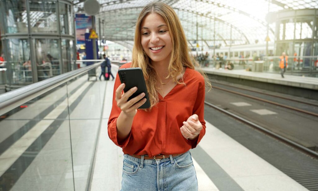 Young smiling woman holding mobile phone on sun flare platform s