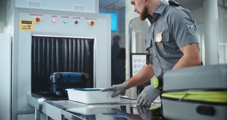 Security Officer Putting Suitcases and Personal Items in Trays on Conveyor Belt with X-ray Scanning