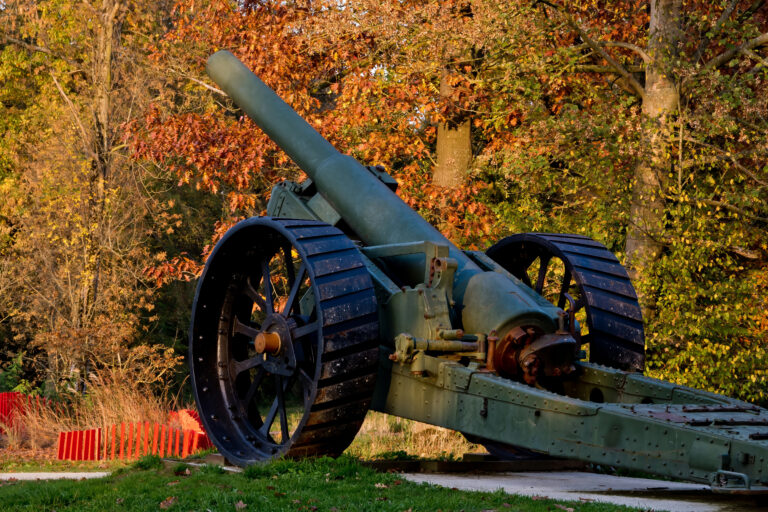 Fall landscape in Flanders Fields. WW1 artillery cannon displayed outdoors against backdrop of vibrant autumn foliage.