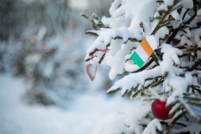 Ireland flag. Christmas background outdoor. Christmas tree covered with snow and decorations and Irish flag.  New Year / Christmas holiday greeting card.